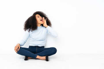 Young african american woman sitting on the floor shouting with mouth wide open to the lateral