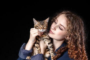 Young beautiful woman with bengal cat on black background