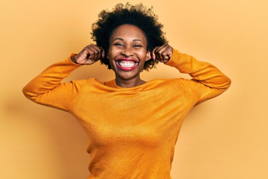 Young african american woman wearing casual clothes smiling pulling ears with fingers, funny gesture. audition problem