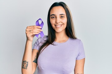Young hispanic woman holding purple ribbon awareness looking positive and happy standing and...