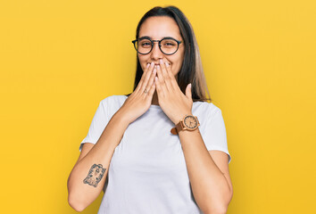 Young hispanic woman wearing casual white t shirt laughing and embarrassed giggle covering mouth...