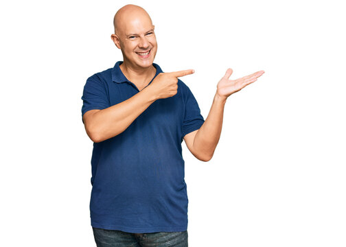 Middle age bald man wearing casual clothes amazed and smiling to the camera while presenting with hand and pointing with finger.