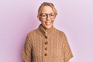 Middle age blonde woman wearing glasses over pink background with a happy and cool smile on face. lucky person.