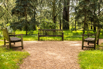 Three garden benches on a gravel path in a park.