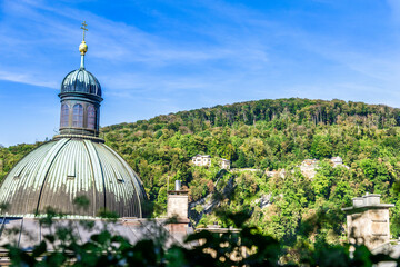 The green dome of the Salzburg Cathedral against a blue sky and tree covered hill in Salzburg...