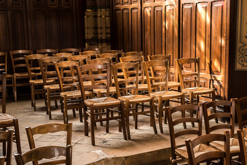 Wood chairs with woven wicker seats are sunlit in a church.