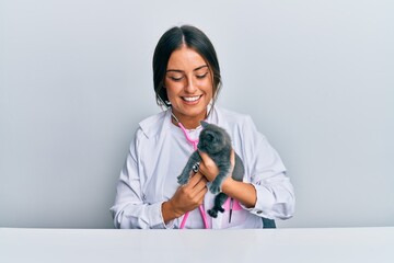 Young hispanic veterinary girl examining cat using stethoscope at the clinic.
