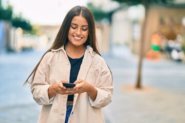 Young hispanic girl smiling happy using smartphone at the city.
