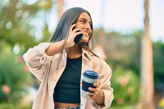 Young hispanic girl smiling happy talking on the smartphone and drinking take away coffee at the park.