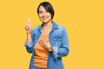Young beautiful hispanic woman with short hair wearing casual denim jacket smiling swearing with hand on chest and fingers up, making a loyalty promise oath