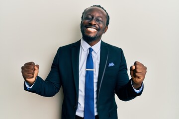 Handsome young black man wearing business suit and tie very happy and excited doing winner gesture with arms raised, smiling and screaming for success. celebration concept.