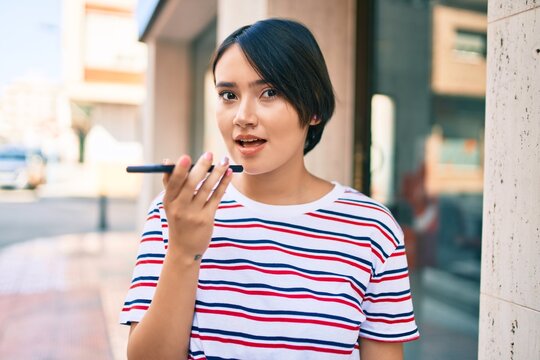 Young latin girl smiling happy sending voice message using smartphone at the city