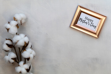 Happy Mother's Day text in rose gold frame with cotton on gray background.  Greeting card concept spring flowers flat lay.