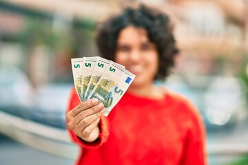 Young hispanic woman smiling happy holding 5 euro banknotes at the city.