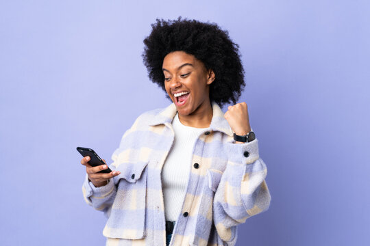 Young African American woman using mobile phone isolated on purple background celebrating a victory