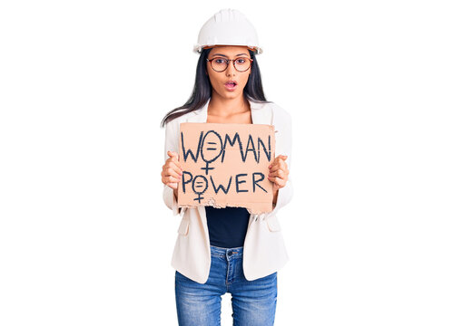 Young beautiful latin girl wearing architect hardhat holding woman power banner scared and amazed with open mouth for surprise, disbelief face