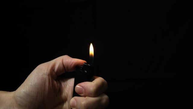Hand burning flame with a lighter in the dark, black night background, portable device used to create a flame