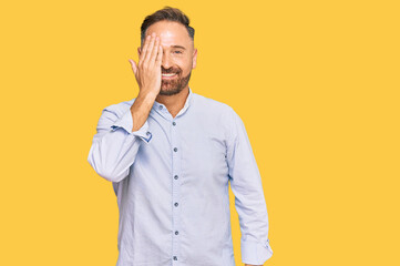 Handsome middle age man wearing business shirt covering one eye with hand, confident smile on face and surprise emotion.