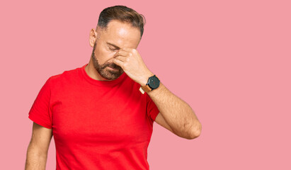 Handsome middle age man wearing casual red tshirt tired rubbing nose and eyes feeling fatigue and headache. stress and frustration concept.