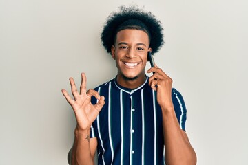 African american man with afro hair having conversation talking on the smartphone doing ok sign with fingers, smiling friendly gesturing excellent symbol