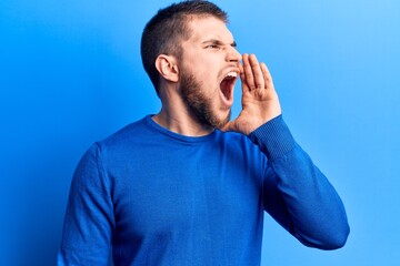 Young handsome man wearing casual sweater shouting and screaming loud to side with hand on mouth. communication concept.