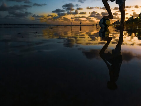 Pé de uma criança sobre bola de futebol na praia no fim da tarde. - Powered by Adobe
