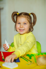 a little beautiful girl makes an application of colored paper