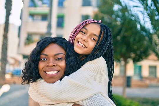 Beautiful african american mother giving daughter piggyback ride smiling happy at the park.