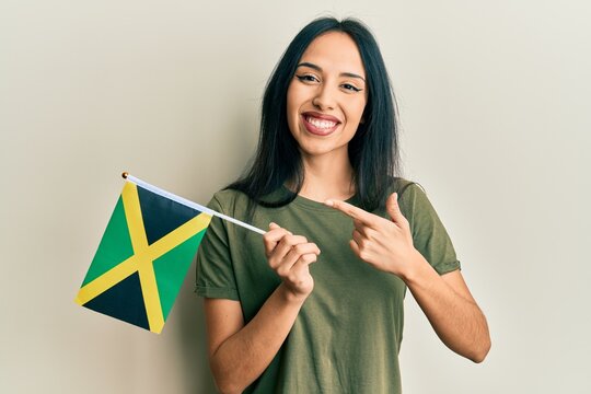 Young hispanic girl holding jamaica flag smiling happy pointing with hand and finger