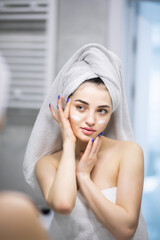 Attractive girl putting anti-aging cream on her face after shower in bathroom