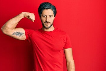 Fototapeta premium Young hispanic man wearing casual red t shirt strong person showing arm muscle, confident and proud of power