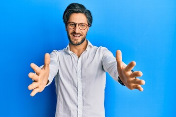 Young hispanic man wearing casual clothes and glasses looking at the camera smiling with open arms for hug. cheerful expression embracing happiness.