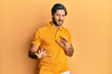 Young hispanic man wearing casual yellow t shirt disgusted expression, displeased and fearful doing disgust face because aversion reaction. with hands raised