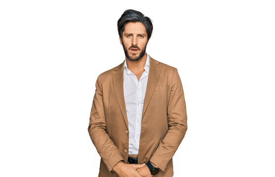 Young hispanic man wearing business clothes in shock face, looking skeptical and sarcastic, surprised with open mouth