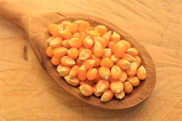 Close-up of a wooden spoon full of corn with raw wood as background. 