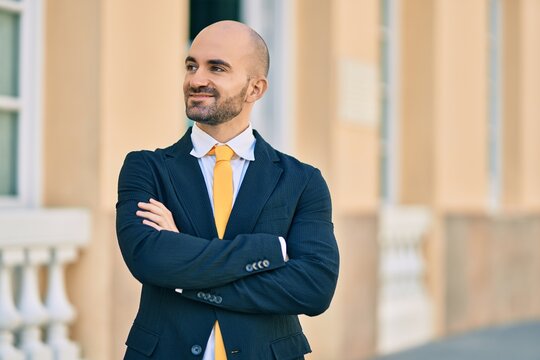 Young hispanic bald businessman with arms crossed smiling happy at the city.