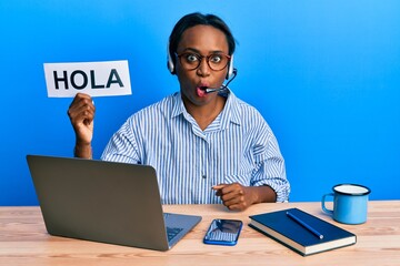 Young african woman wearing operator headset holding hola word scared and amazed with open mouth for surprise, disbelief face © Krakenimages.com