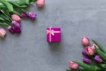Pink gift box and tulips on a gray concrete background. Copyspace. Postcard, Gift.