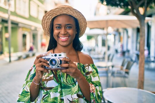 Young african american tourist woman on vacation smiling happy using vintage camera at the city.