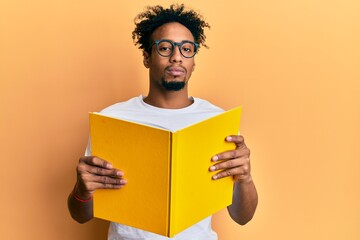 Young african american man with beard reading a book wearing glasses relaxed with serious expression on face. simple and natural looking at the camera.