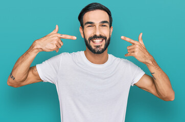 Young hispanic man wearing casual white t shirt smiling cheerful showing and pointing with fingers teeth and mouth. dental health concept.