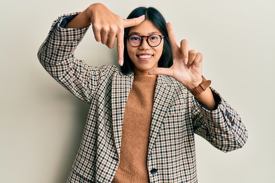 Young chinese woman wearing business style and glasses smiling making frame with hands and fingers with happy face. creativity and photography concept.