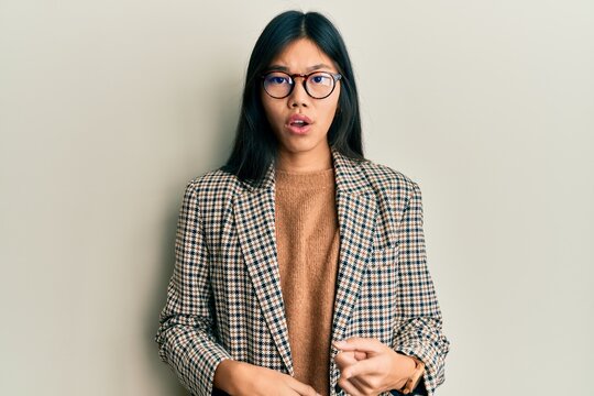 Young chinese woman wearing business style and glasses surprised pointing with finger to the side, open mouth amazed expression.