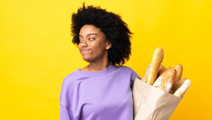 Young African American woman buying something bread isolated on yellow background . Portrait