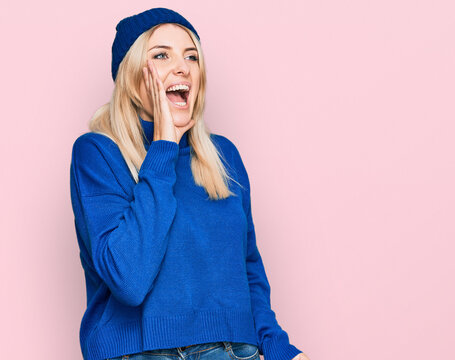 Young caucasian woman wearing wool winter sweater and cap shouting and screaming loud to side with hand on mouth. communication concept.