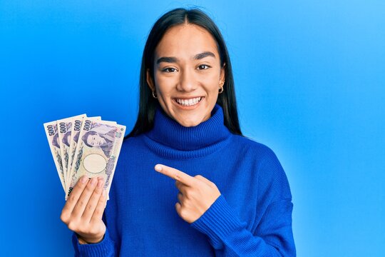 Young asian woman holding 5000 japanese yen banknotes smiling happy pointing with hand and finger