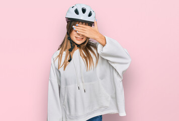 Teenager caucasian girl wearing bike helmet smiling and laughing with hand on face covering eyes for surprise. blind concept.
