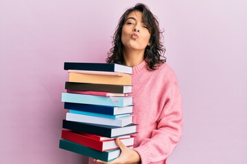 Young hispanic woman holding a pile of books looking at the camera blowing a kiss being lovely and sexy. love expression.