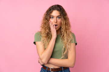 Young blonde woman with curly hair isolated on pink background surprised and shocked while looking right