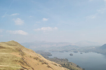 Looking across the yellow side of a mountain top, across a beautiful rural valley to a wide lake in a haze. Misty day viewing Derwent Water, the Lake District, England UK